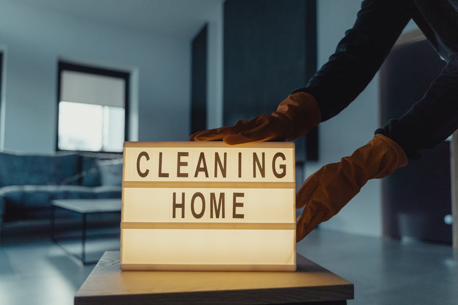 A soft gray wall features a small, pale blue wall hook holding a wooden-handled scrub brush with natural bristles and a light-colored cleaning cloth draped over the brush's handle. The surface of the 